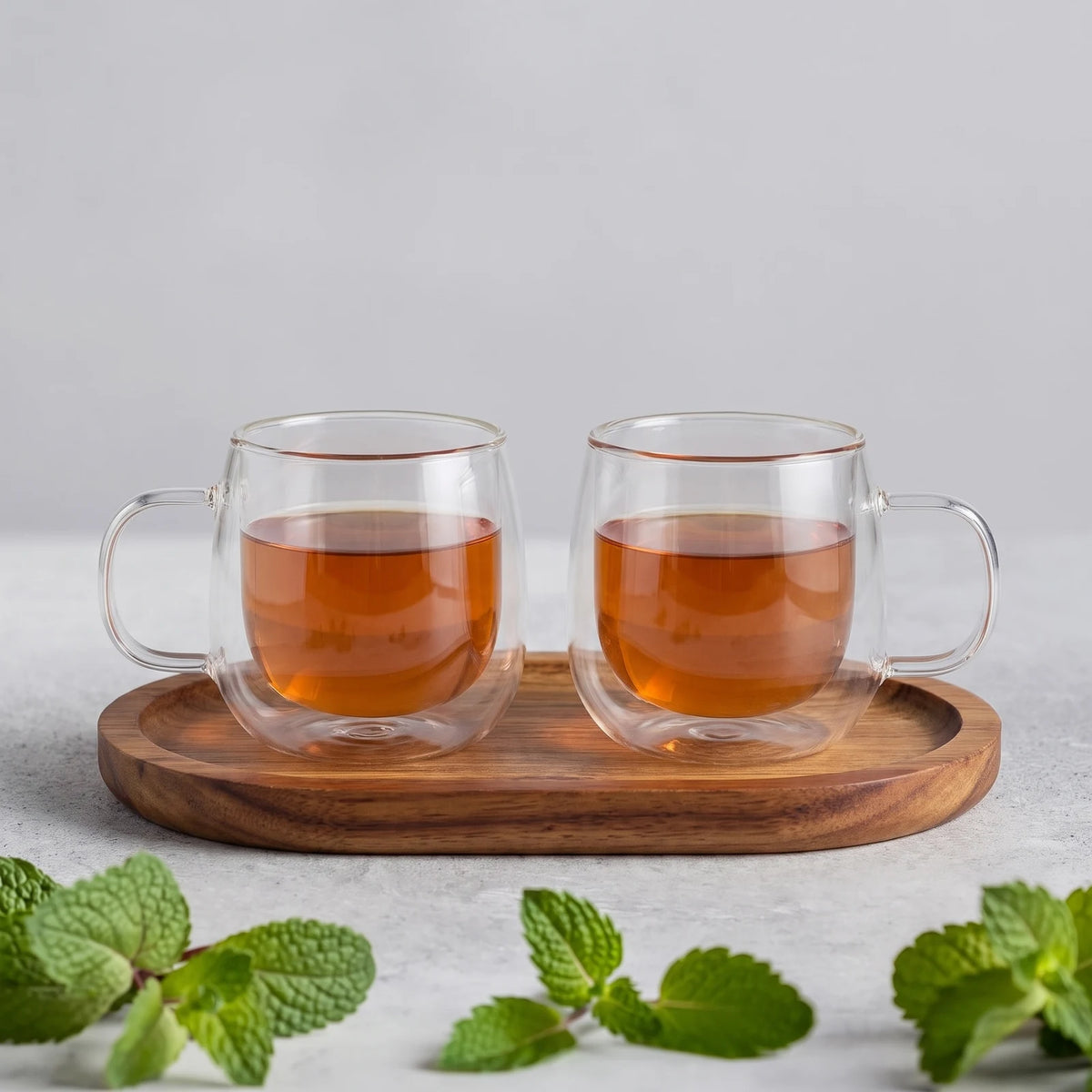 Zwei doppelwandige Glastassen mit Tee auf dem Holzbrettchen