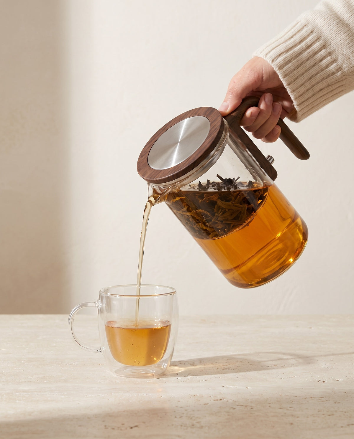 Tee wird aus der Glas-Teekanne in eine Glastasse eingeschenkt